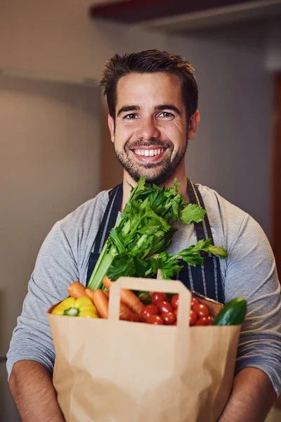 Daha iyi yediğinde daha iyi hissedersin. Mutfağında bir torba yiyecekle poz veren mutlu bir gencin portresi.. — Stok fotoğraf