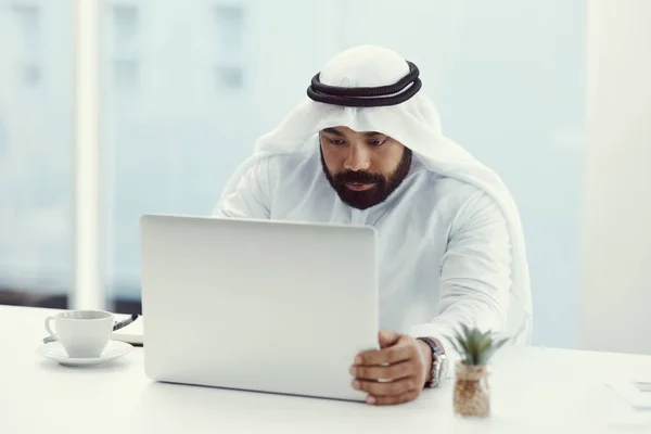 Focused on the task at hand. Cropped shot of a young businessman dressed in Islamic traditional clothing working on his laptop while sitting in the office. — Stock Photo, Image