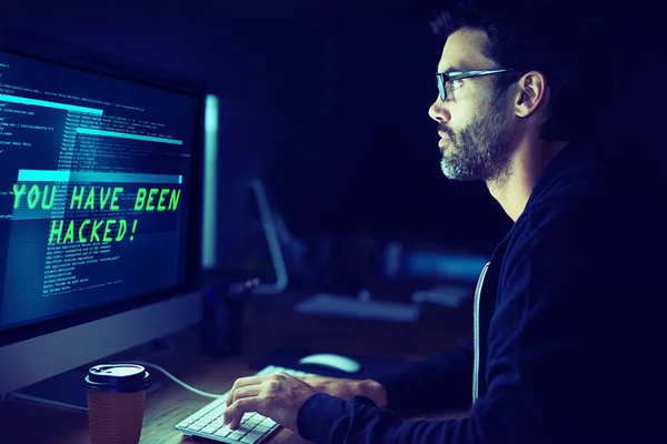 Hij kan achter je aan komen. Opname van een gerichte computer hacker met behulp van een computer in het donker. — Stockfoto