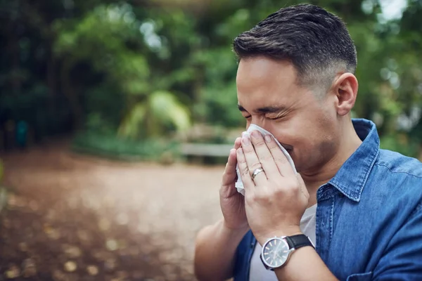 Its the season of sneezes again. Cropped shot of a young man blowing his nose with a tissue outdoors. — Stock Photo, Image