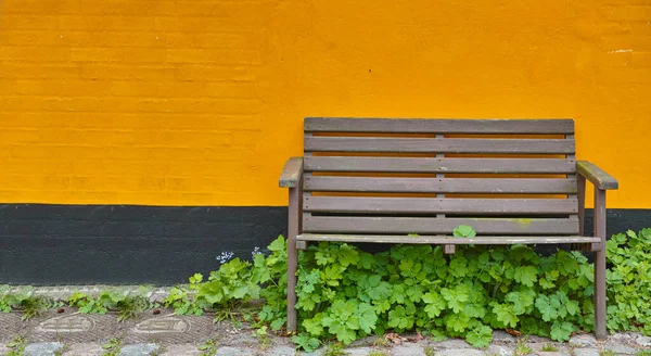 Sente-se.... Um único banco de madeira contra uma parede laranja brilhante. — Fotografia de Stock