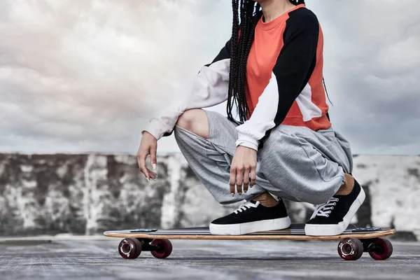 Me ven rodando... Cortada el tiro de una joven patinadora irreconocible agachada en su longboard en una azotea contra un telón de fondo tormentoso. — Foto de Stock