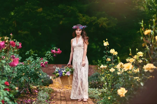 Folgen Sie dem Blumenpfad, um die besten Blumen zu pflücken. Aufnahme einer schönen jungen Frau mit einem Blumenkranz und einem Korb voller Blumen in der Natur. — Stockfoto