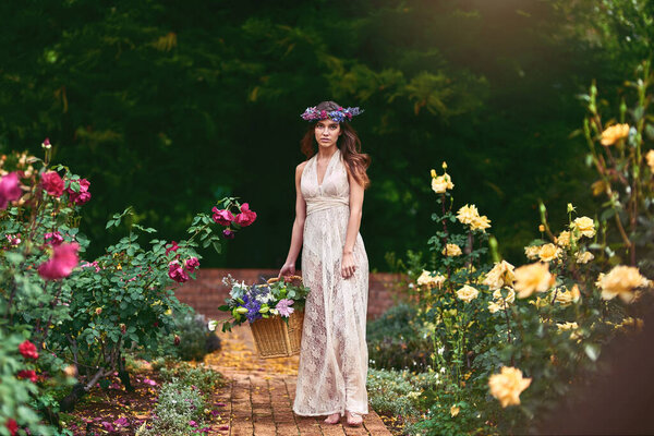 Shot of a beautiful young woman wearing a floral head wreath and holding a basket full of flowers in nature.
