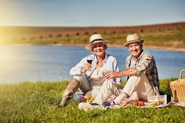 El amor nos mantiene jóvenes de corazón. Toma de una feliz pareja de ancianos bebiendo vino mientras disfruta de un picnic al aire libre. — Foto de Stock