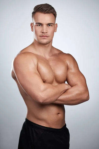 Du kan inte fejka kondition. Studio porträtt av en muskulös ung man poserar med armarna korsade mot en grå bakgrund. — Stockfoto