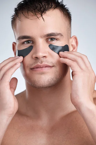 Age comes for everyone. Closeup portrait of a young handsome man wearing an under-eye charcoal patch against a grey background. — Stock Photo, Image