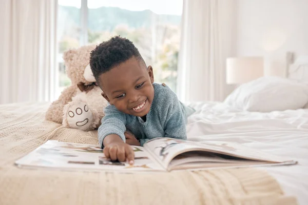 Uwielbia czytać. Całkowite ujęcie uroczego chłopca czytającego książkę na łóżku w domu. — Zdjęcie stockowe
