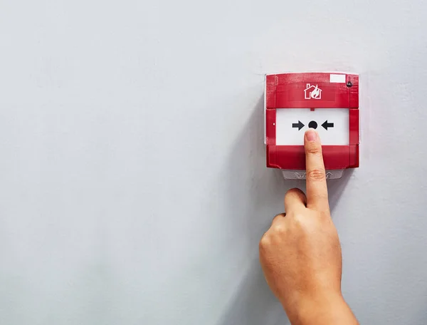 Activeer het alarm. Gehakt schot van een persoon die een brandalarm op een muur drukt. — Stockfoto