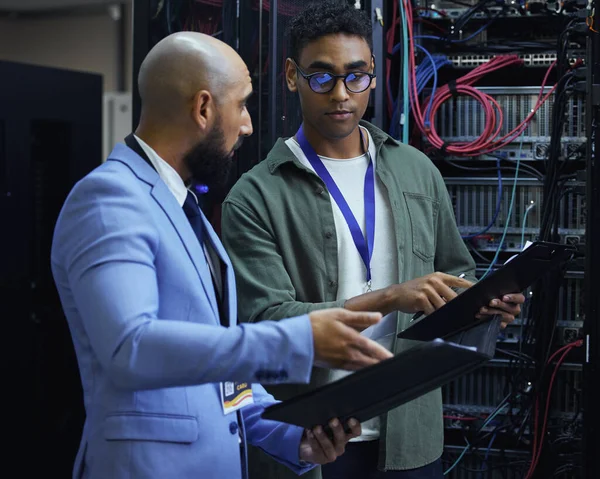 Ik bekijk het diagnostisch rapport. Gesneden opname van twee mannelijke IT-ondersteuningsagenten die samenwerken in een donkere netwerkserverruimte. — Stockfoto