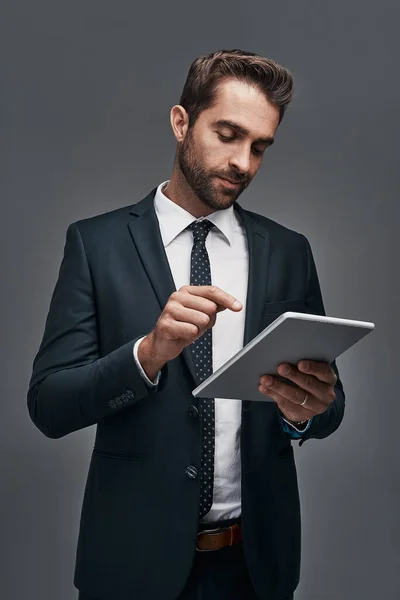 Gekoppeld aan het bedrijfsleven. Studio shot van een knappe jonge zakenman met behulp van een digitale tablet tegen een grijze achtergrond. — Stockfoto