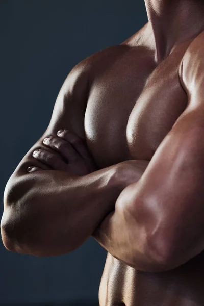 Muscles sur les muscles. Gros plan d'un jeune homme méconnaissable et athlétique poitrine tandis qu'il pose les bras croisés en studio sur un fond sombre. — Photo