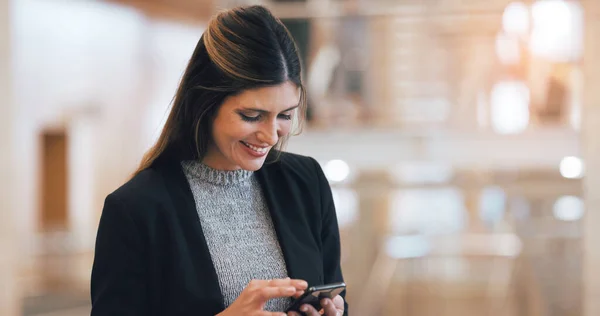 Le encanta recibir comentarios positivos de su equipo. Recorte de una atractiva joven empresaria sonriendo mientras usa el teléfono inteligente en un lugar de trabajo moderno. —  Fotos de Stock