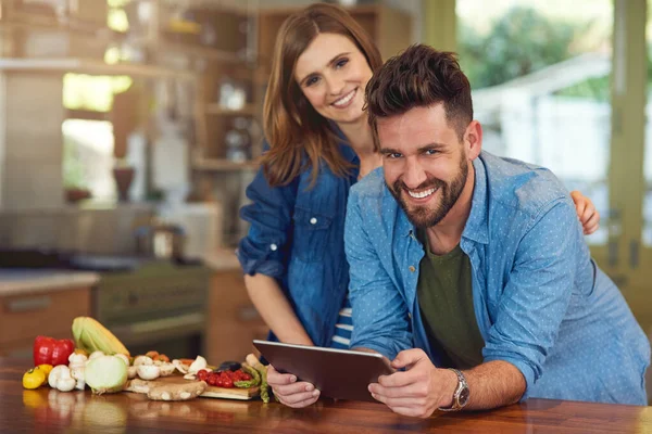 Fazendo planejamento de refeições uma brisa com tecnologia moderna. Retrato de um jovem casal feliz usando um tablet digital enquanto preparam uma refeição saudável juntos em casa. — Fotografia de Stock