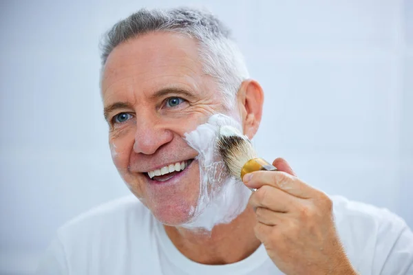 Hoje em dia um dia de cuidados com a pele. Tiro de um homem maduro aplicando creme de barbear em seu rosto em um banheiro em casa. — Fotografia de Stock