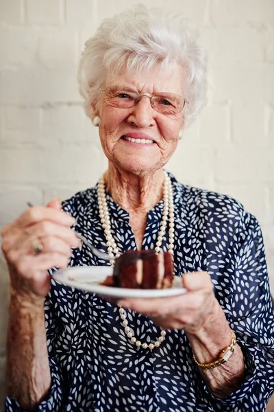 Pensioen staat me goed. Schot van een oudere vrouw die een stuk taart binnen at.. — Stockfoto