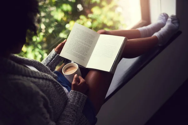 Fuggendo nella narrazione. Girato di una giovane donna non identificabile che legge un libro mentre si gode una tazza di caffè a casa. — Foto Stock