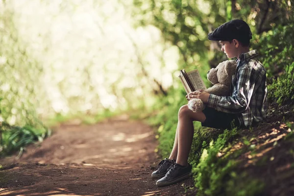 读书和大自然是他最喜欢的两样东西。被一个快乐的小男孩在森林里给他的泰迪熊读书开枪打死了. — 图库照片