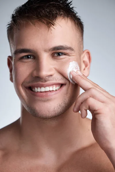 Dont be acting like a punk thinking youre a soldier. Cropped closeup portrait of an attractive young man applying moisturiser to his face against a grey background. — Stock Photo, Image