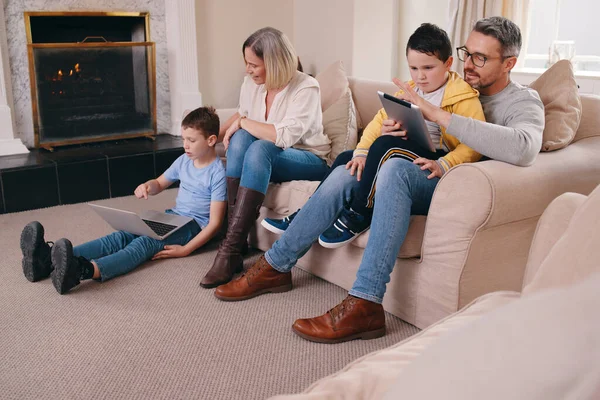Besoin d'un meilleur plan de données. Prise de vue d'une jeune famille collant tout en utilisant leurs appareils électroniques ensemble à la maison. — Photo