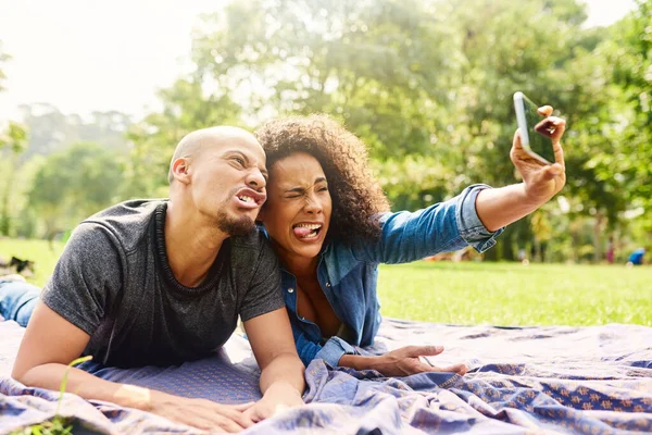 Fai una faccia divertente e mostra il tuo lato divertente. Foto ritagliata di una giovane bella coppia che trascorre la giornata in un parco pubblico. — Foto Stock