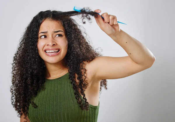 Vorrei ci fosse un modo piu 'semplice per districarmi i capelli. Colpo di una donna accigliata mentre pettina i capelli contro uno sfondo grigio. — Foto Stock