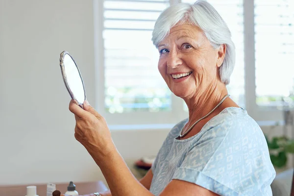 Nog steeds prachtig na al die jaren. Portret van een gelukkige oudere vrouw met behulp van een handspiegel thuis. — Stockfoto