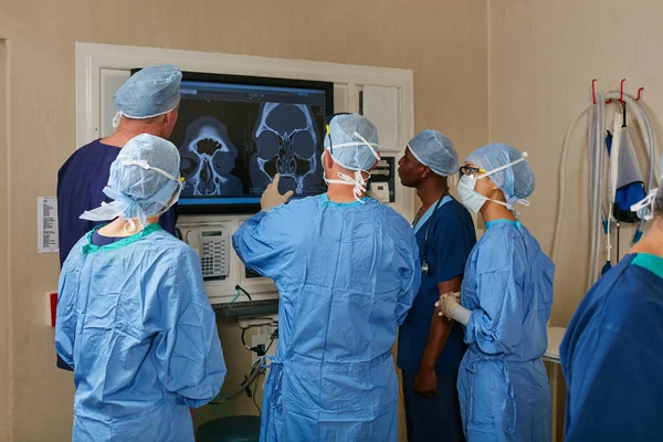 Vi diskuterar deras alternativ. Skjuten av ett team kirurger diskuterar en patient medicinska skanningar under operation. — Stockfoto
