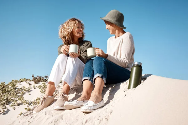 Haciendo de la playa su propio café personal. Largura completa de dos atractivas mujeres maduras disfrutando de un poco de café mientras están sentadas en la playa. — Foto de Stock