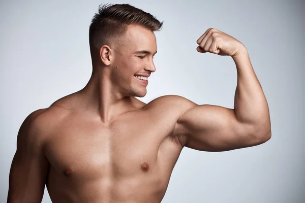 Bombea algo de hierro. Estudio de un joven musculoso flexionando su brazo sobre un fondo gris. — Foto de Stock