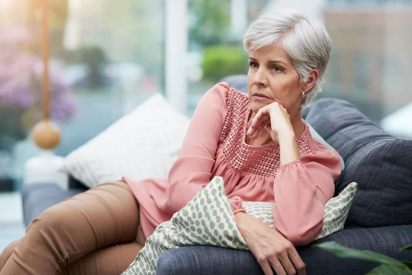 This whole situation Im in is making me angry. Shot of a mature woman looking thoughtful while relaxing on her couch at home. — Stock Photo, Image