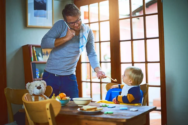 Ο μπαμπάς ξέρει να κάνει πολλές δουλειές. Τραβηγμένο πλάνο ενός μόνο πατέρα σε μια κλήση, ενώ ταΐζει το γιο του στο σπίτι. — Φωτογραφία Αρχείου