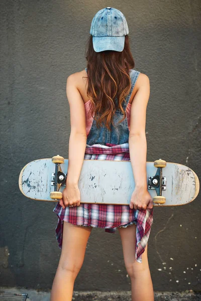 Todo lo que necesitas es tu tabla si eres un patinador. Vista trasera de una joven irreconocible de pie con un monopatín detrás de su espalda sobre un fondo gris. —  Fotos de Stock