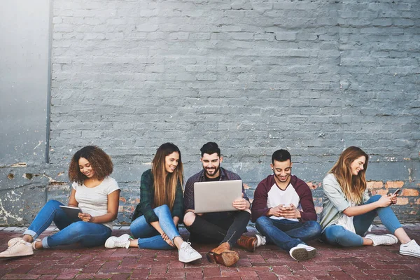 Conectarse en una era conectada. Fotografía de un grupo de jóvenes amigos que utilizan sus dispositivos inalámbricos juntos al aire libre. —  Fotos de Stock