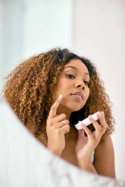 Μόνο λίγο από αυτό εδώ και εκεί. Shot of a confident young woman applying skin cream on her face ενώ κοιτάζεται στον καθρέφτη στο μπάνιο στο σπίτι. — Φωτογραφία Αρχείου