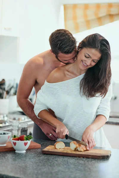 Qué está cocinando, guapo. Shot de un joven cariñoso abrazando a su novia por detrás mientras ella hace el desayuno en la cocina. — Foto de Stock
