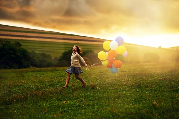 Žvanit po polích. Postřelen hravé holčičky, která běhá po poli a drží balónky. — Stock fotografie