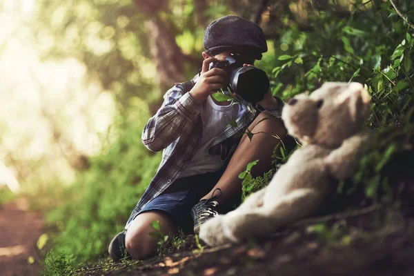 Er ist der süßeste kleine Fotograf. Aufnahme eines nicht identifizierbaren Jungen, der mit einer Kamera Fotos von seinem Teddy im Wald macht. — Stockfoto