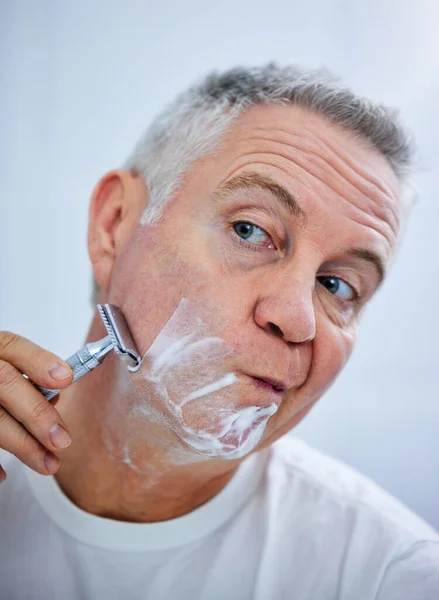 I have to concentrate when shaving. Shot of a mature man shaving his face in a bathroom at home. — Stock Photo, Image