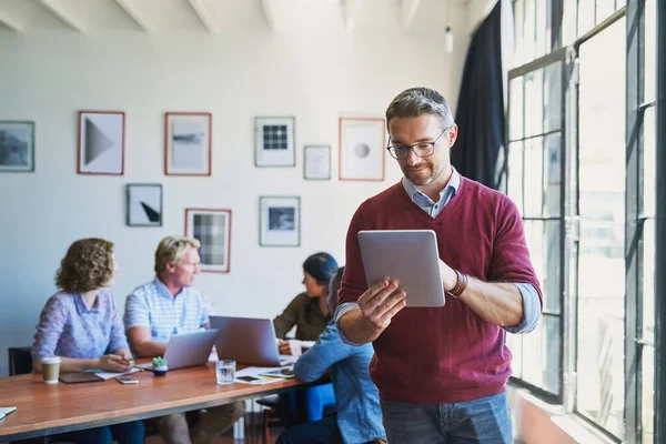 Der digitale Manager erledigt die Dinge. Aufnahme eines reifen Mannes mit einem digitalen Tablet und seinem Team im Hintergrund eines modernen Büros. — Stockfoto