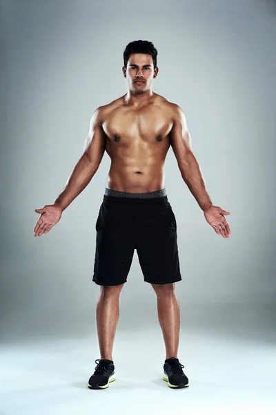 Dit is waarom ik train. Full length portret van een sportieve jongeman staande tegen een grijze achtergrond. — Stockfoto