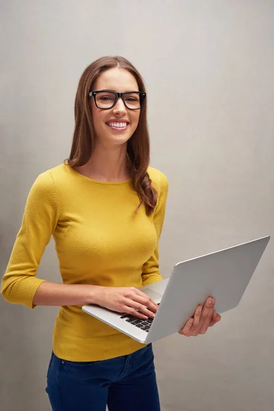 Siempre estoy conectado. Retrato de estudio de una atractiva joven posando con su portátil sobre un fondo gris. — Foto de Stock