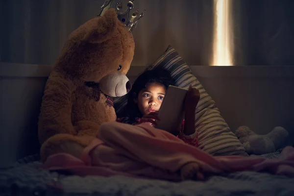 Guardando i suoi cartoni animati preferiti prima di andare a letto. Girato di una bambina che usa un tablet digitale mentre è sdraiata a letto con il suo orsacchiotto di notte. — Foto Stock