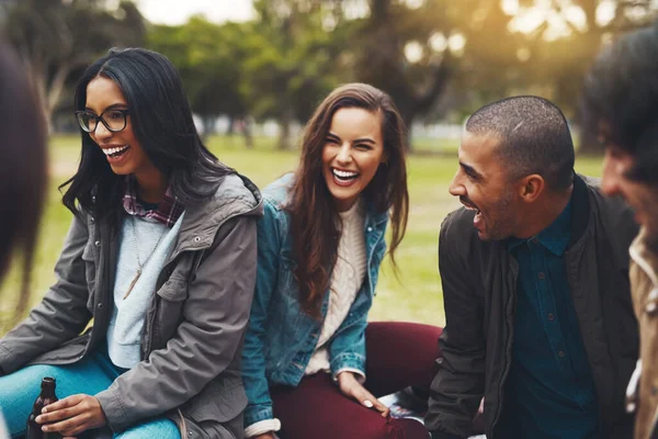 Rimo-nos sempre juntos. Tiro de um grupo de jovens amigos alegres que fazem um piquenique juntos lá fora em um parque durante o dia. — Fotografia de Stock