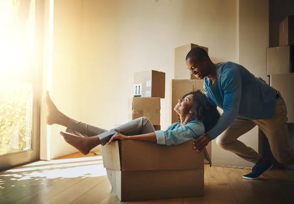 Go faster. Shot of a cheerful young man pushing his girlfriend around in a cardboard box at home during moving day. — Stock Photo, Image