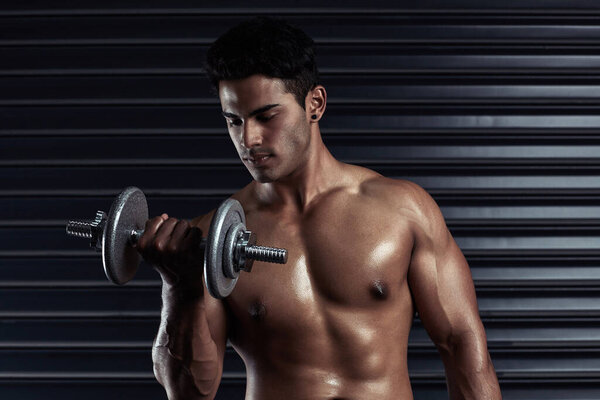 Building his body. Cropped shot of an athletic young man working out with a dumbbell.