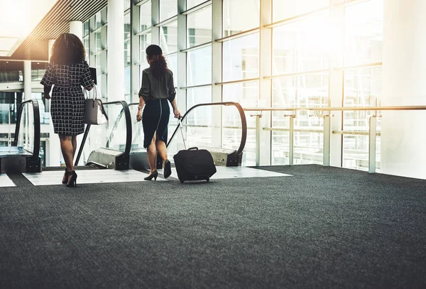 İş seni nereye çağırırsa oraya gitmelisin. Modern bir iş yerinde yürüyen merdivene binen tanınmayan iki iş kadınının dikiz görüntüsü. — Stok fotoğraf