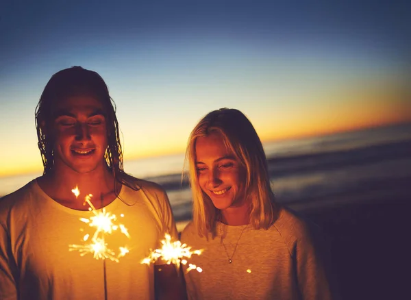 Fira natten. Skjuten av ett ungt par leker med tomtebloss på stranden på natten. — Stockfoto