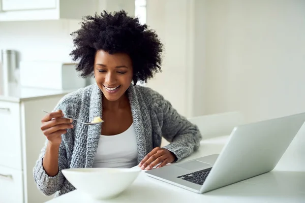 Fueling up for a great day. Shot of a young woman surfing the net while enjoying breakfast in her kitchen at home. — Stock Photo, Image