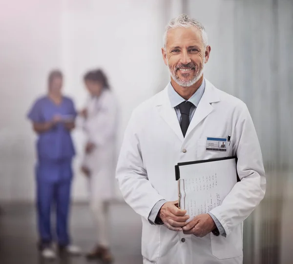 Je travaille pour votre santé. Portrait d'un médecin masculin mature debout dans un hôpital avec ses collègues en arrière-plan. — Photo